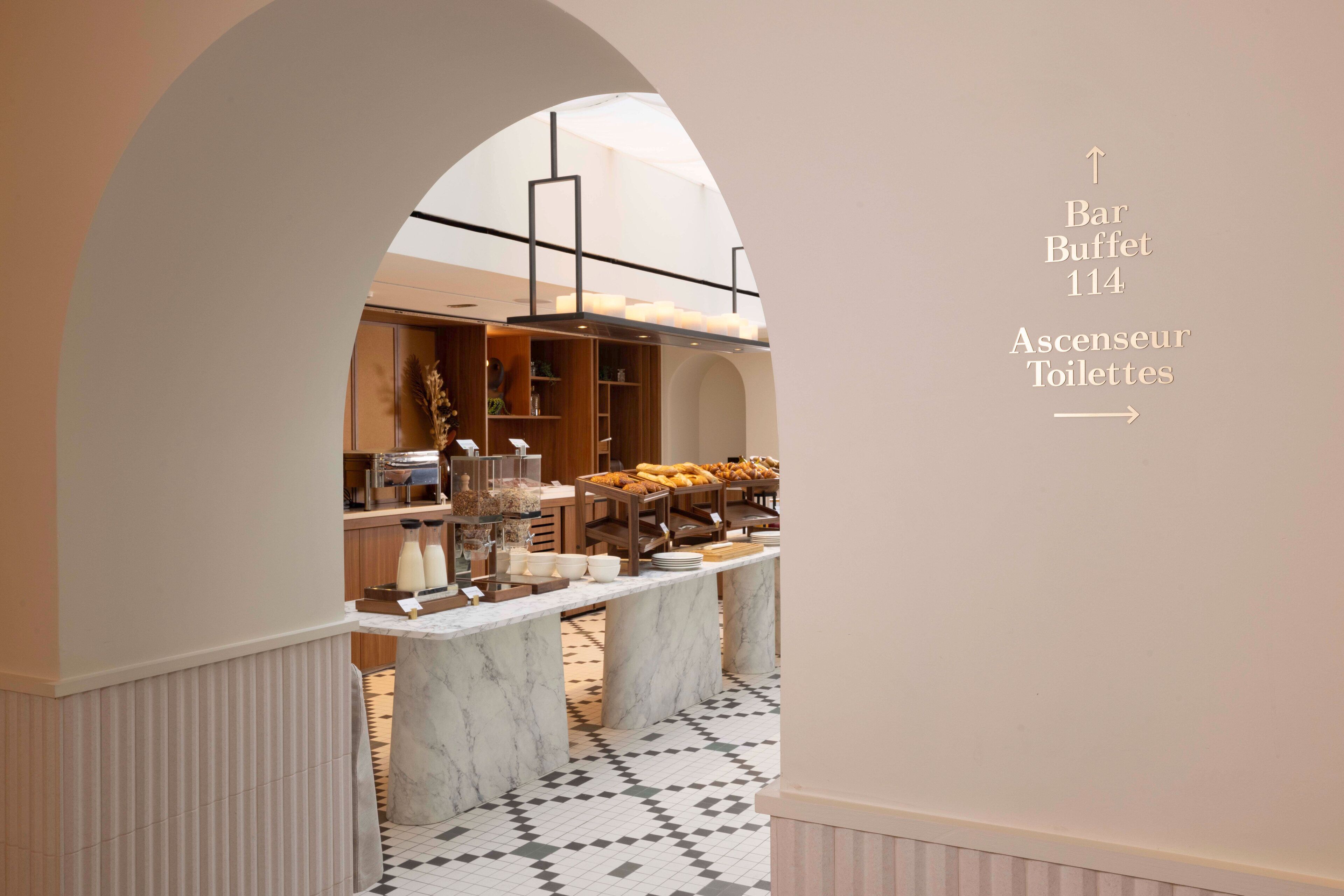 A hotel corridor with a marble counter and a buffet area. Directional signs indicate the locations of the bar buffet and the restroom.