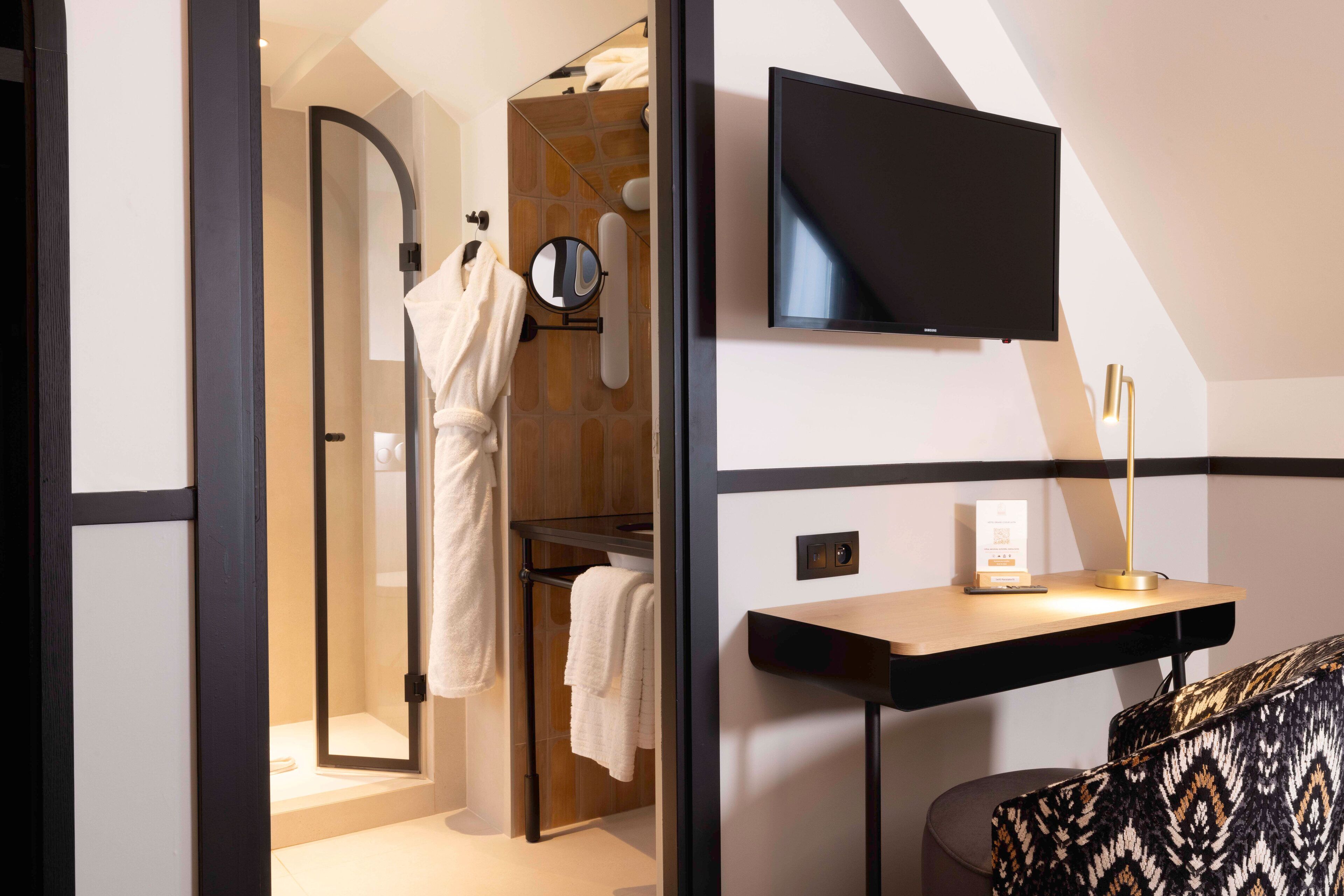 A modern bathroom with a glass shower, a mirror, a towel rack, and a mounted television.