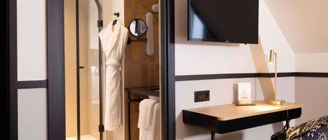 A modern bathroom with a glass shower, a mirror, a towel rack, and a mounted television.
