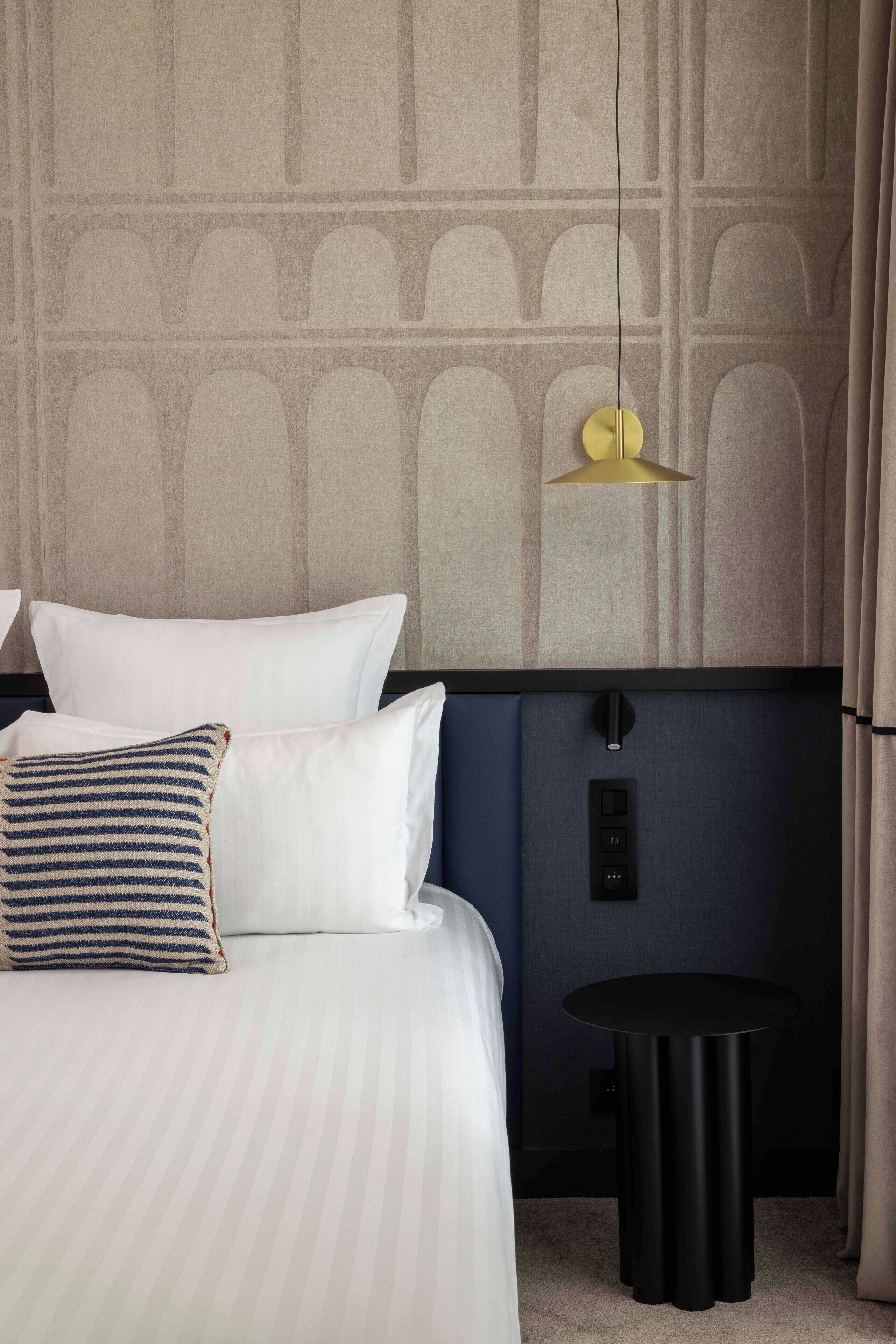 Una habitación de hotel con una cama, una mesita de noche, una lámpara de pared y un panel de control.