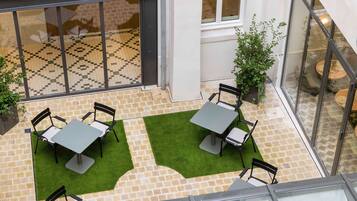 An outdoor patio area with two tables and four chairs, surrounded by a tiled floor and a glass enclosure.