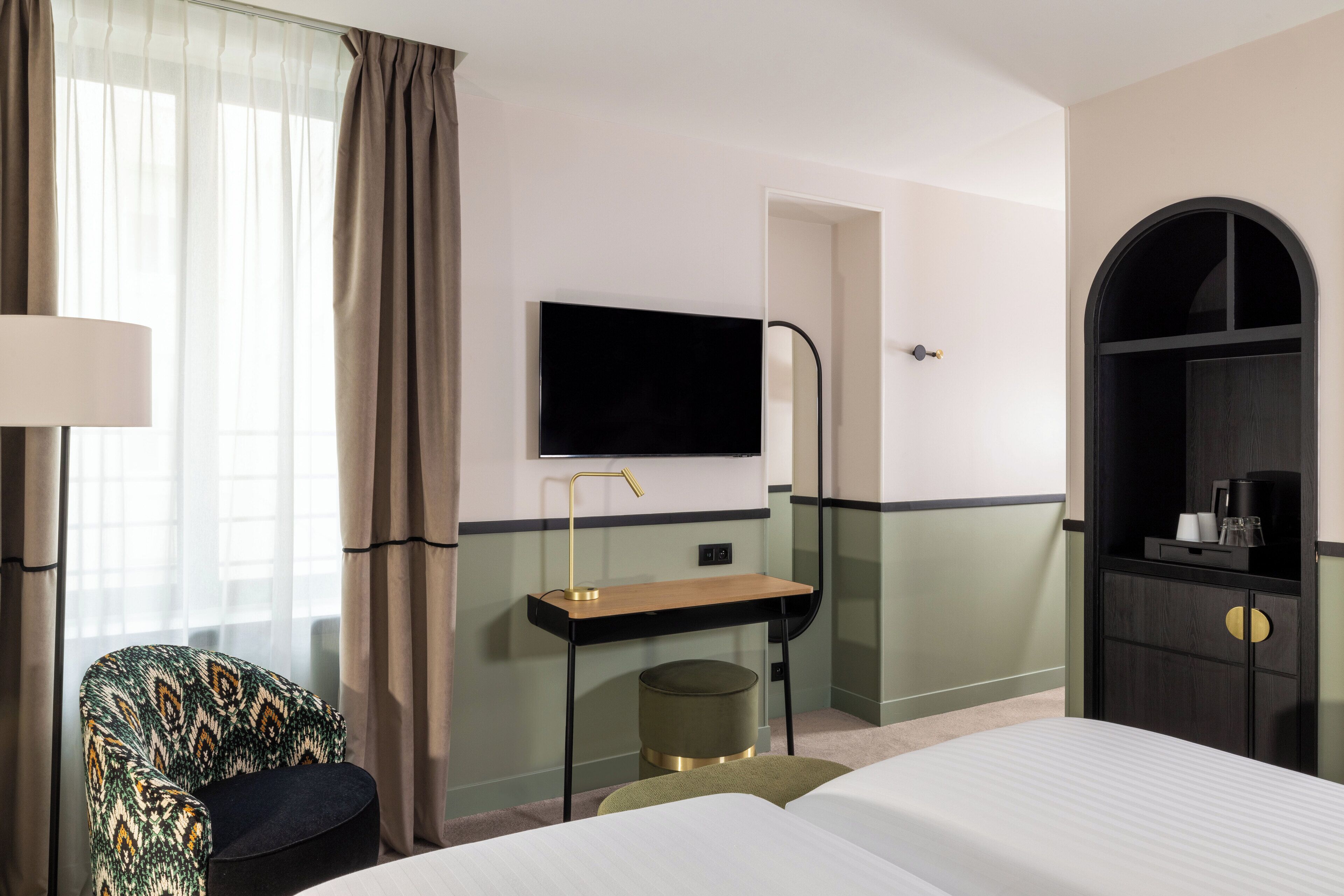 A hotel room with a bed, a desk with a flat-screen TV, a chair, and a wardrobe.