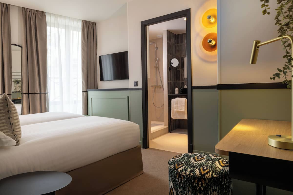 A hotel room with a bed, a desk, a chair, a TV, a shower area, and a bathroom.