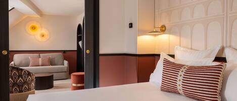 Een hotelkamer met een bed, een bank, een gestreept voetenbankje en een wandlamp.