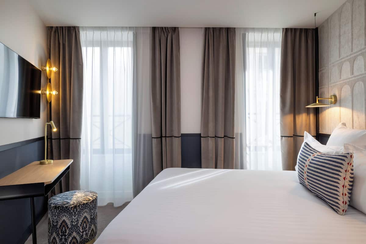A hotel room with a bed, a desk, a chair, and a television.