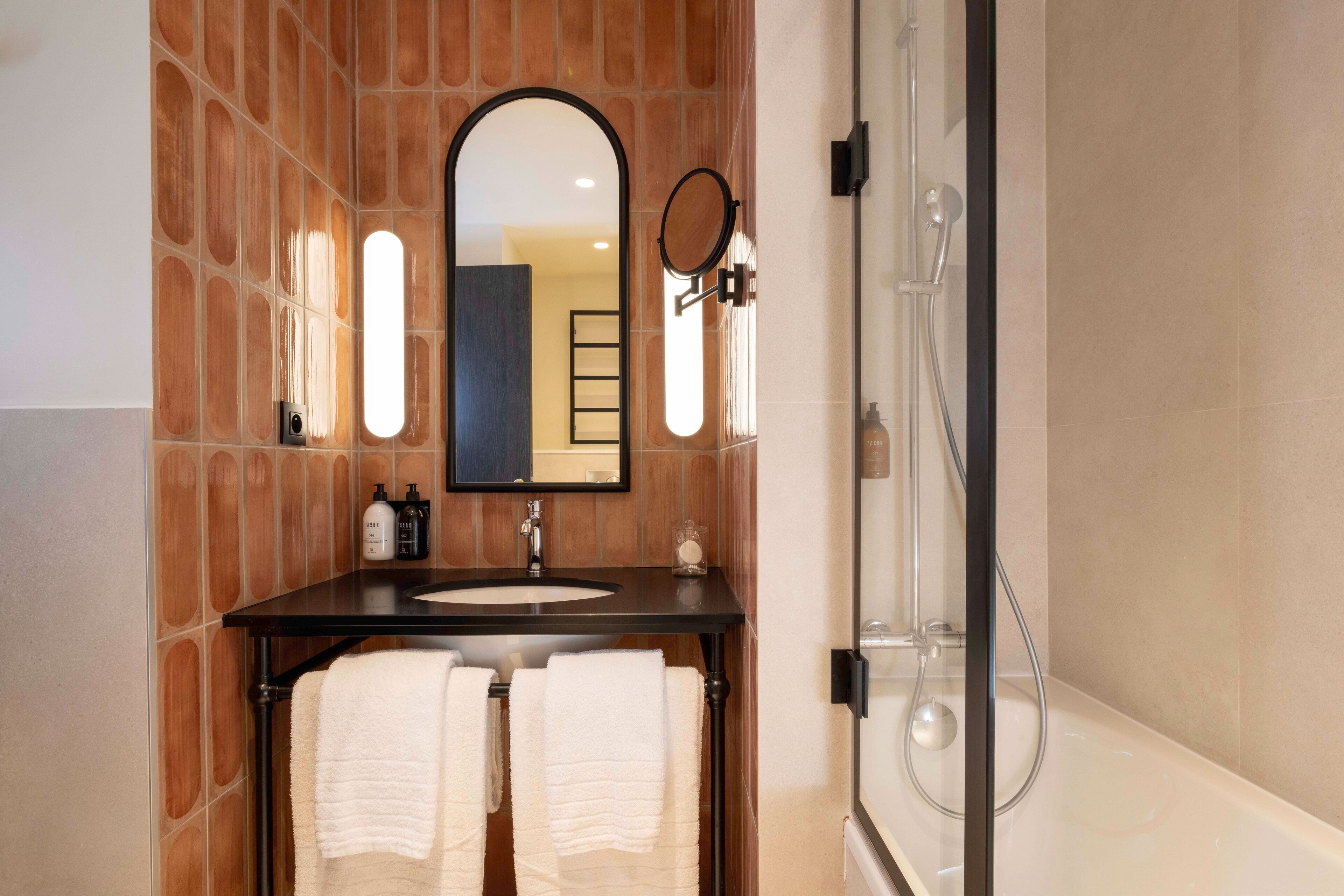 A bathroom with a black sink, two white towels, a mirror, and a glass-enclosed shower.