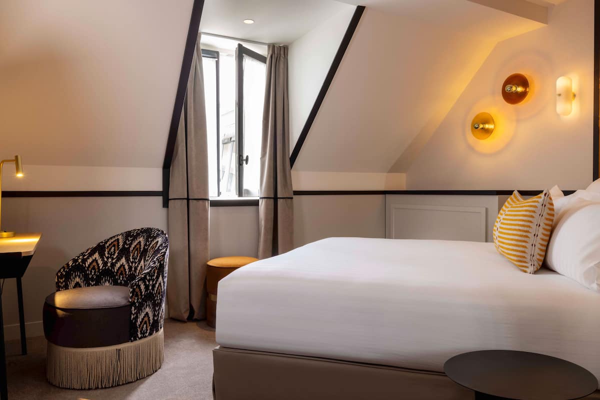 A modern hotel room with a large bed, a chair, a small table, and a view of the outdoors.