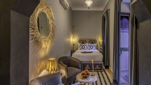 A modern bedroom with a bed, two armchairs, a small table with fruit, a decorative mirror, and a chandelier. - Riad Irhalne (Marrakech)