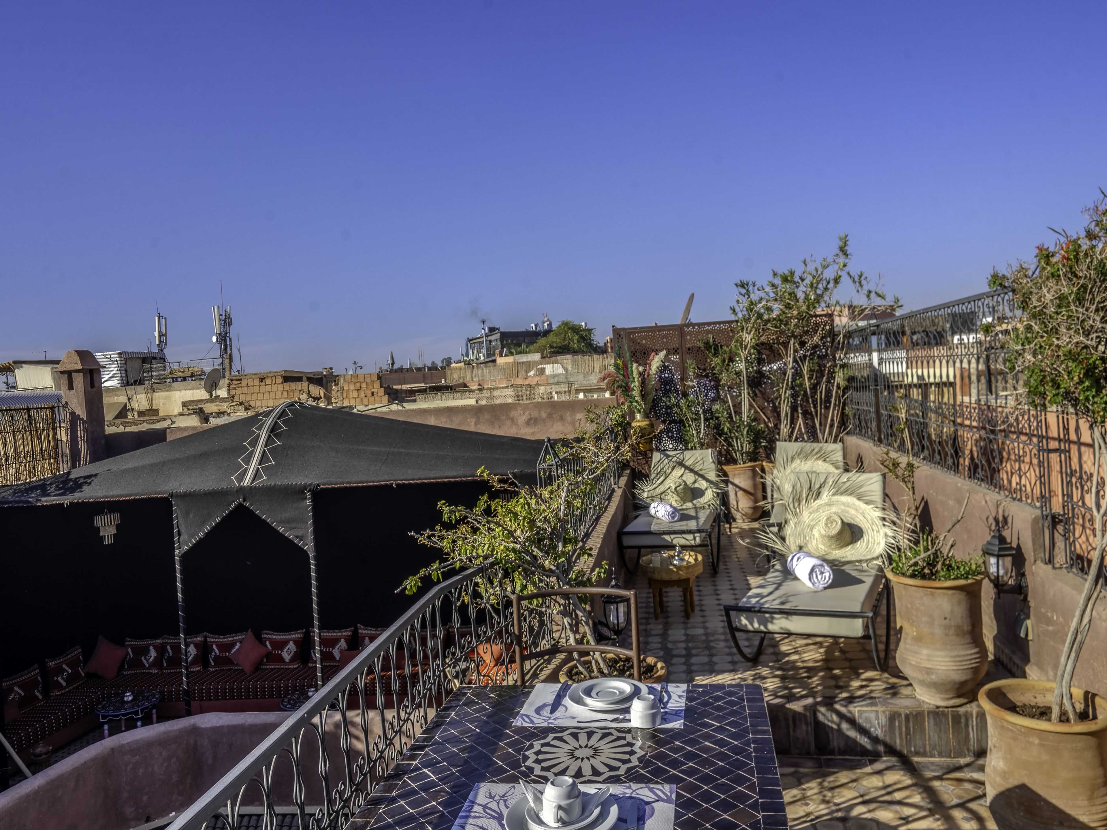 A rooftop terrace with a patterned table, potted plants, and a view of the cityscape.