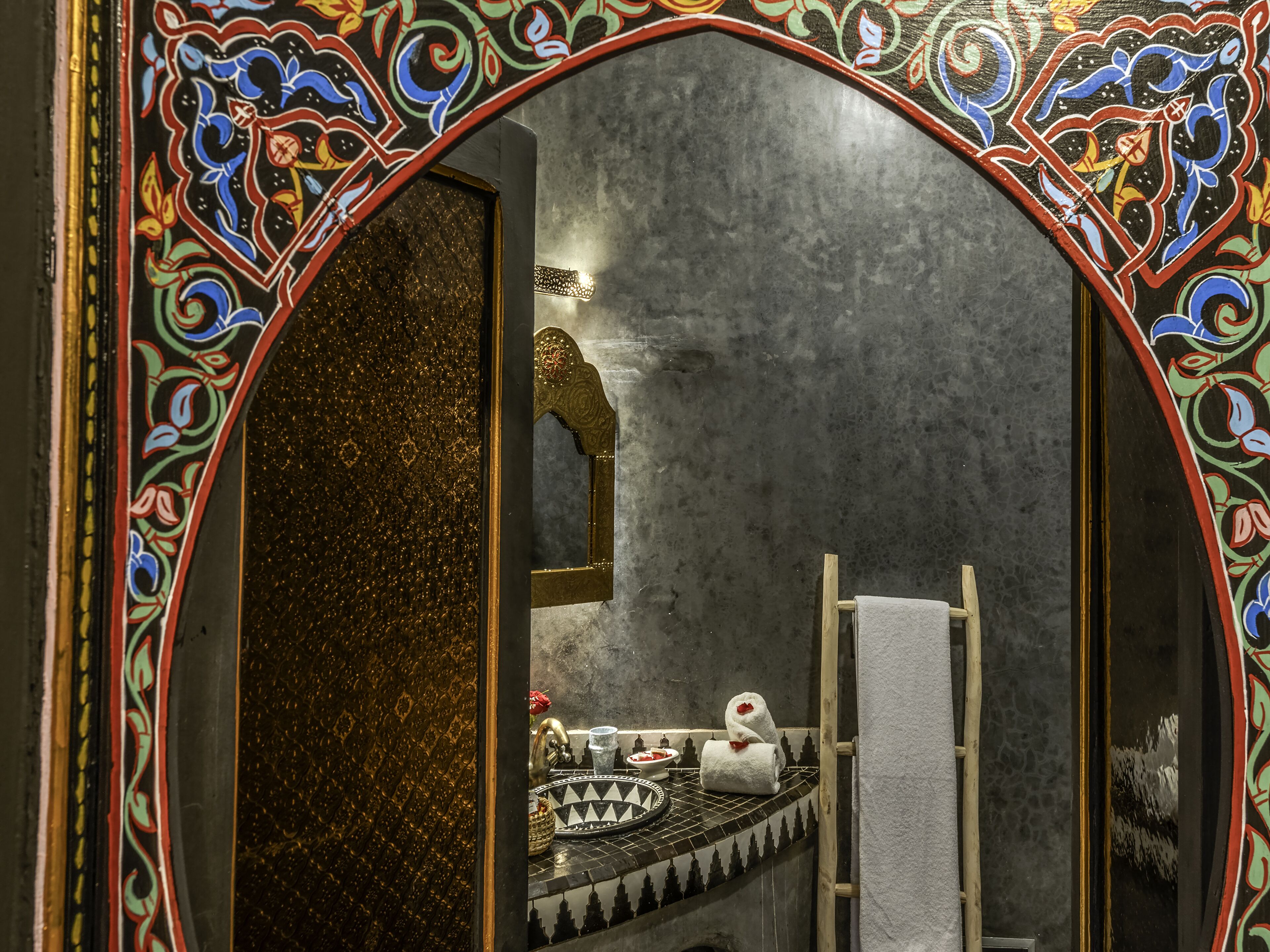 A bathroom with a decorative arch, a mirror, a towel rack, and a sink with a patterned tile backsplash.