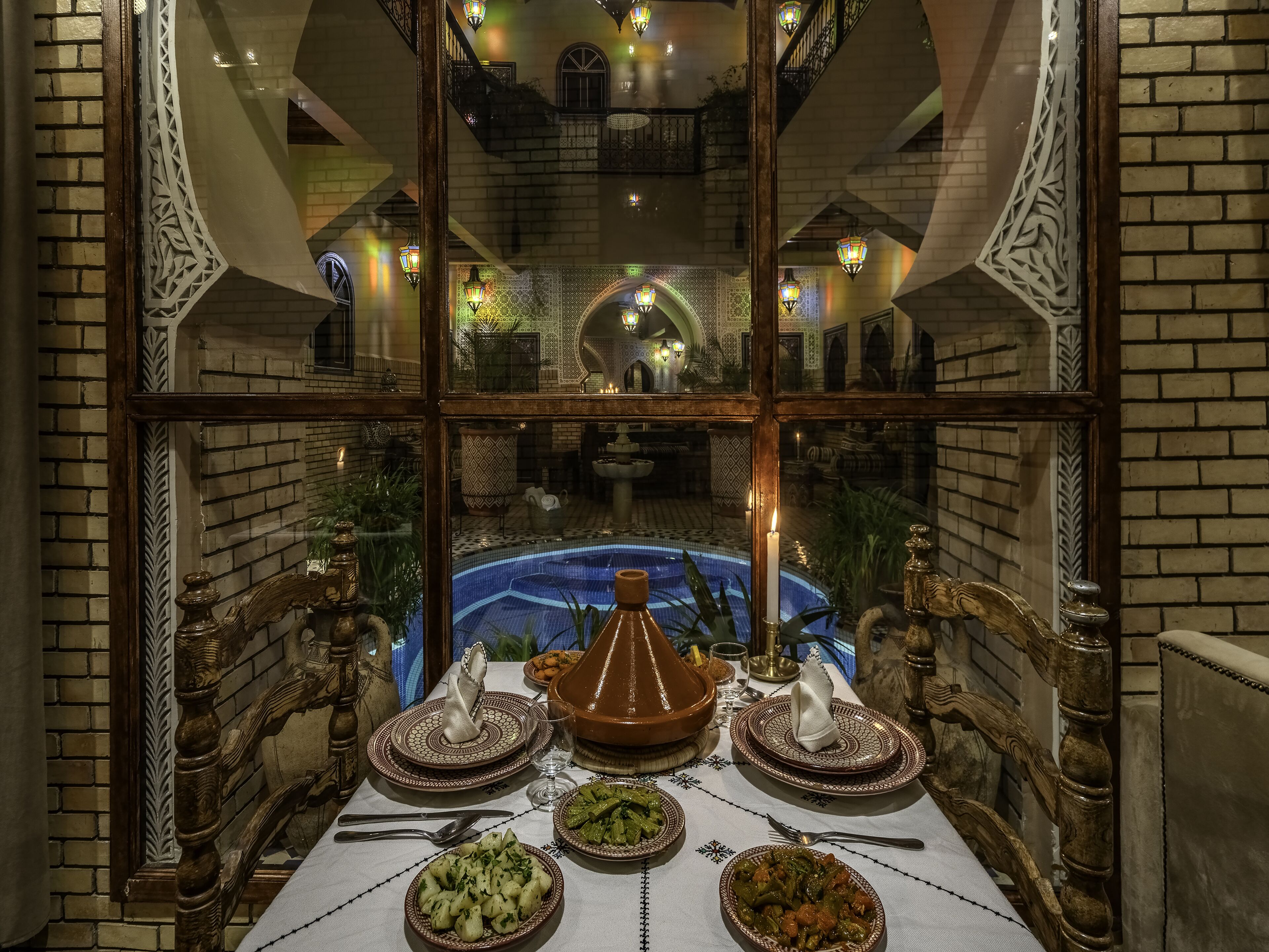 Un espace repas avec vue sur la piscine, décoré dans le style marocain, avec une table dressée de plats traditionnels et un grand vase.