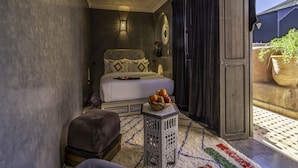 A bedroom with a bed, a nightstand, a small table with fruit, and a view of the outside. - Riad Irhalne (Marrakech)