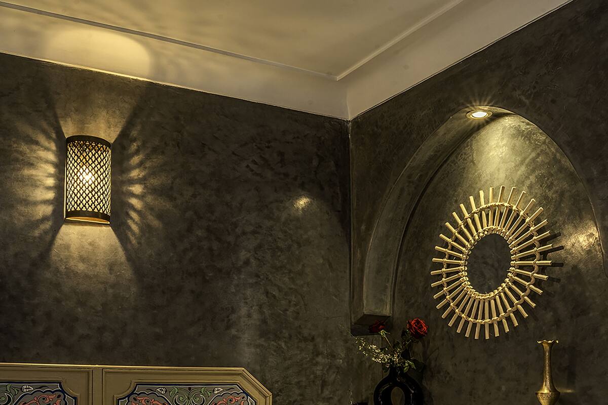 A bedroom with a bed, pillows, a vase with flowers, and a wall-mounted mirror.
