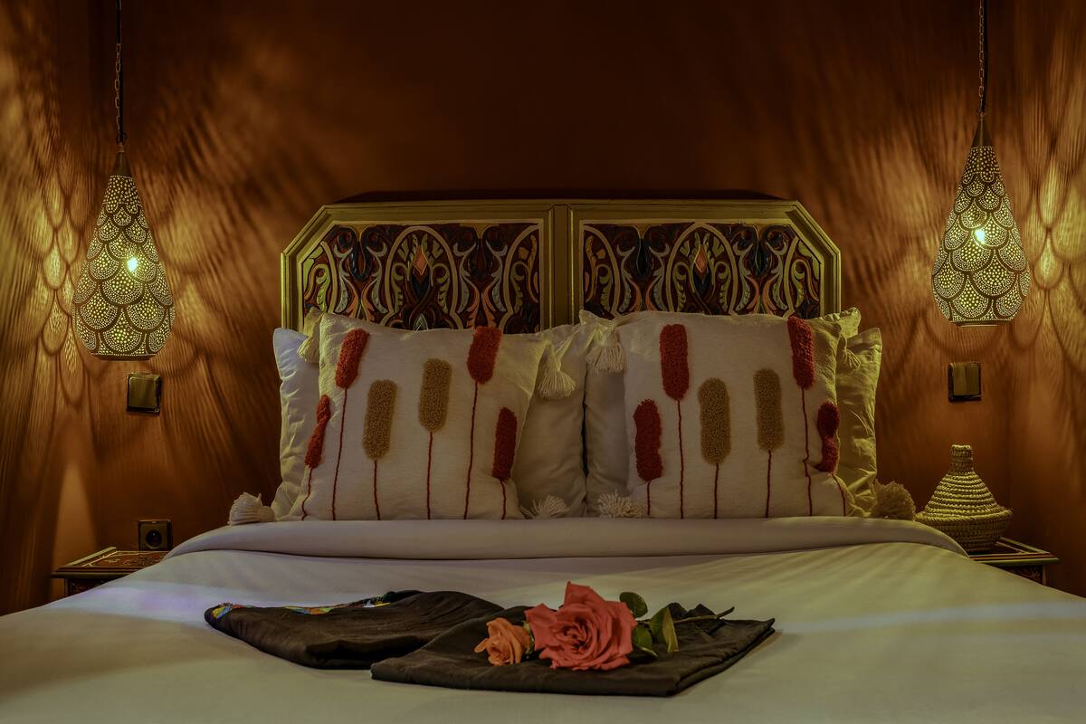 A neatly made bed with decorative pillows and a rose on the bedspread.