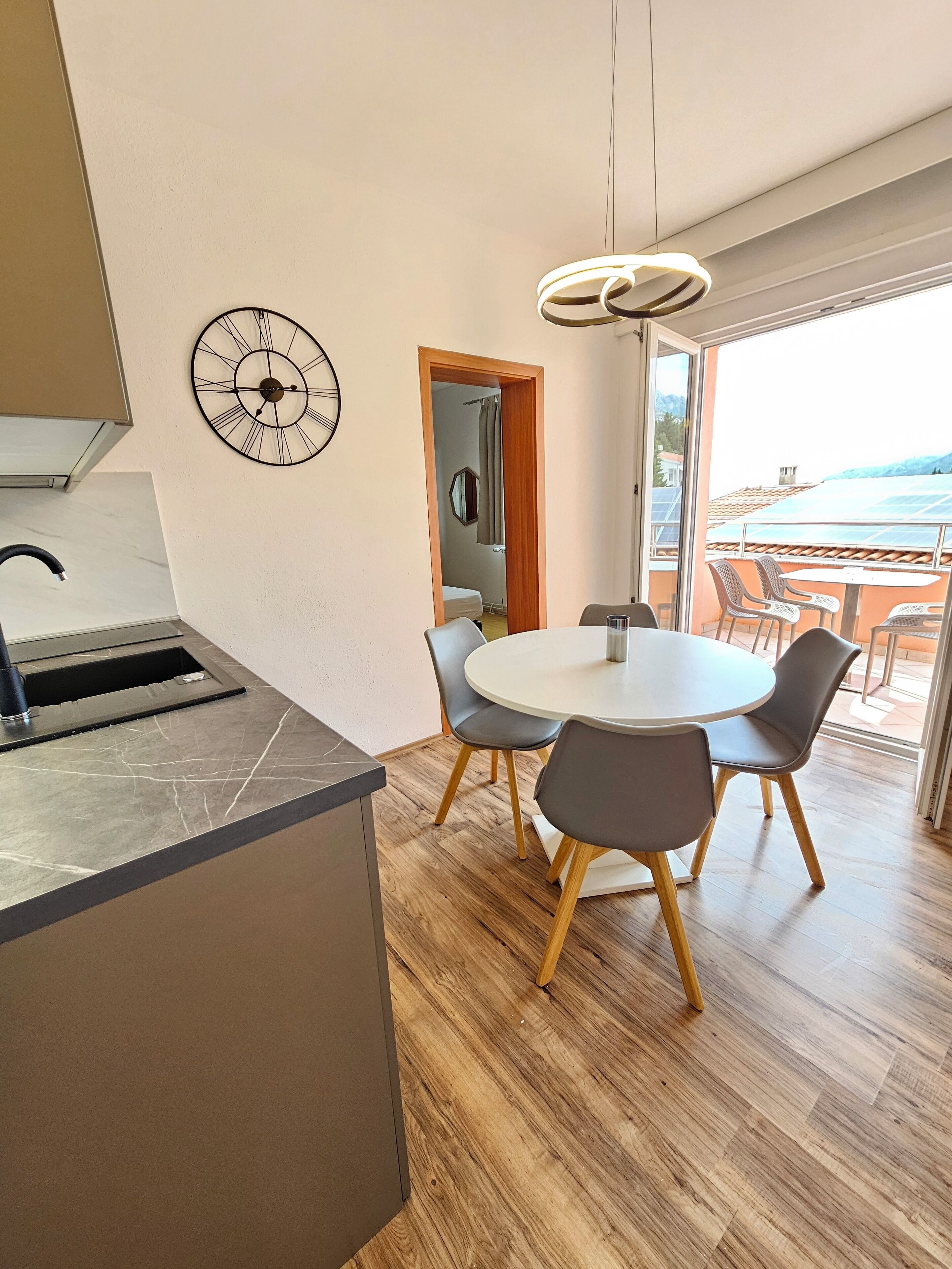 A modern kitchen with a built-in island, a round dining table with chairs, and a large window overlooking a scenic view.