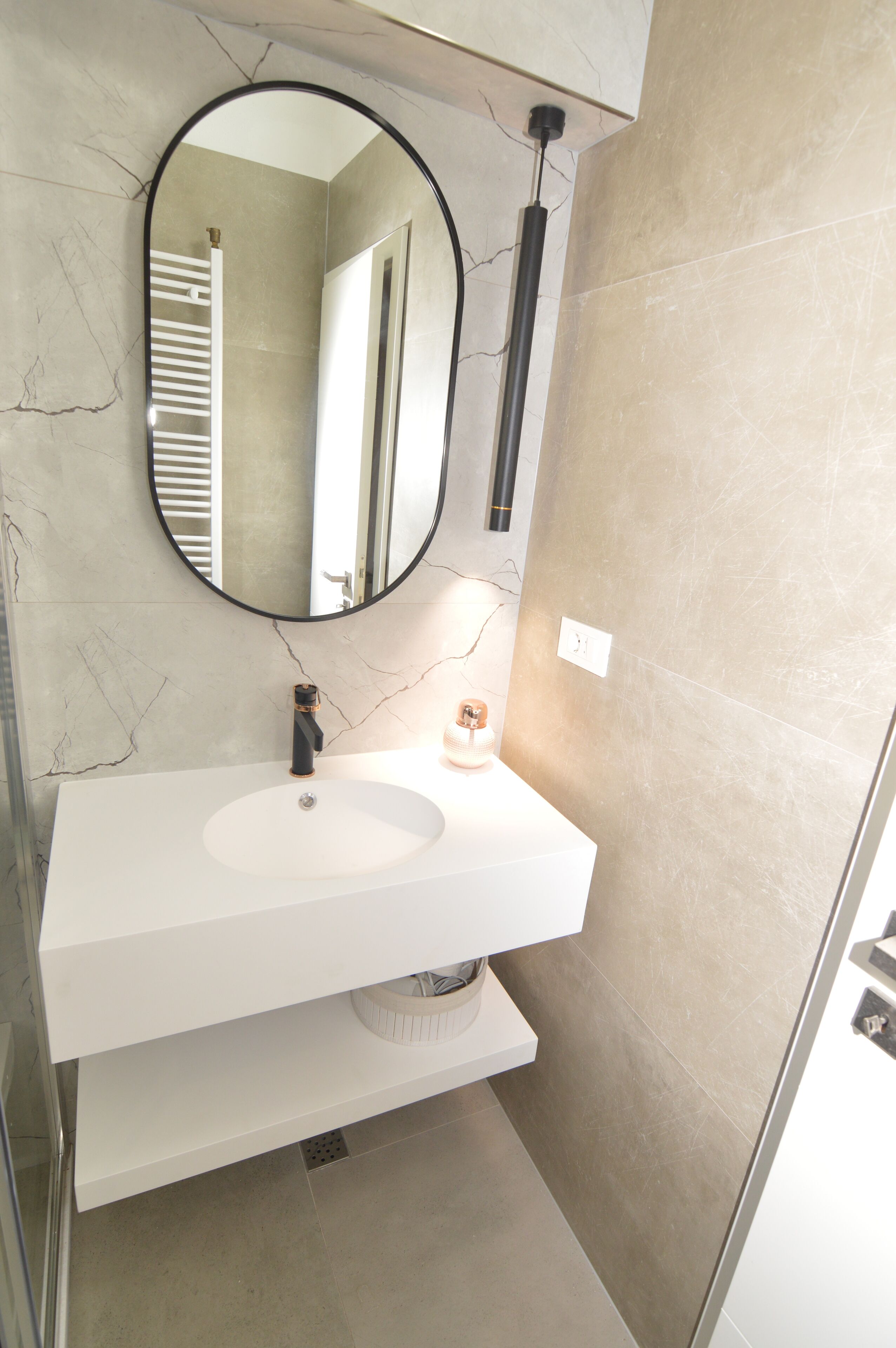 A modern bathroom with a white sink, a round mirror, and a towel rack.