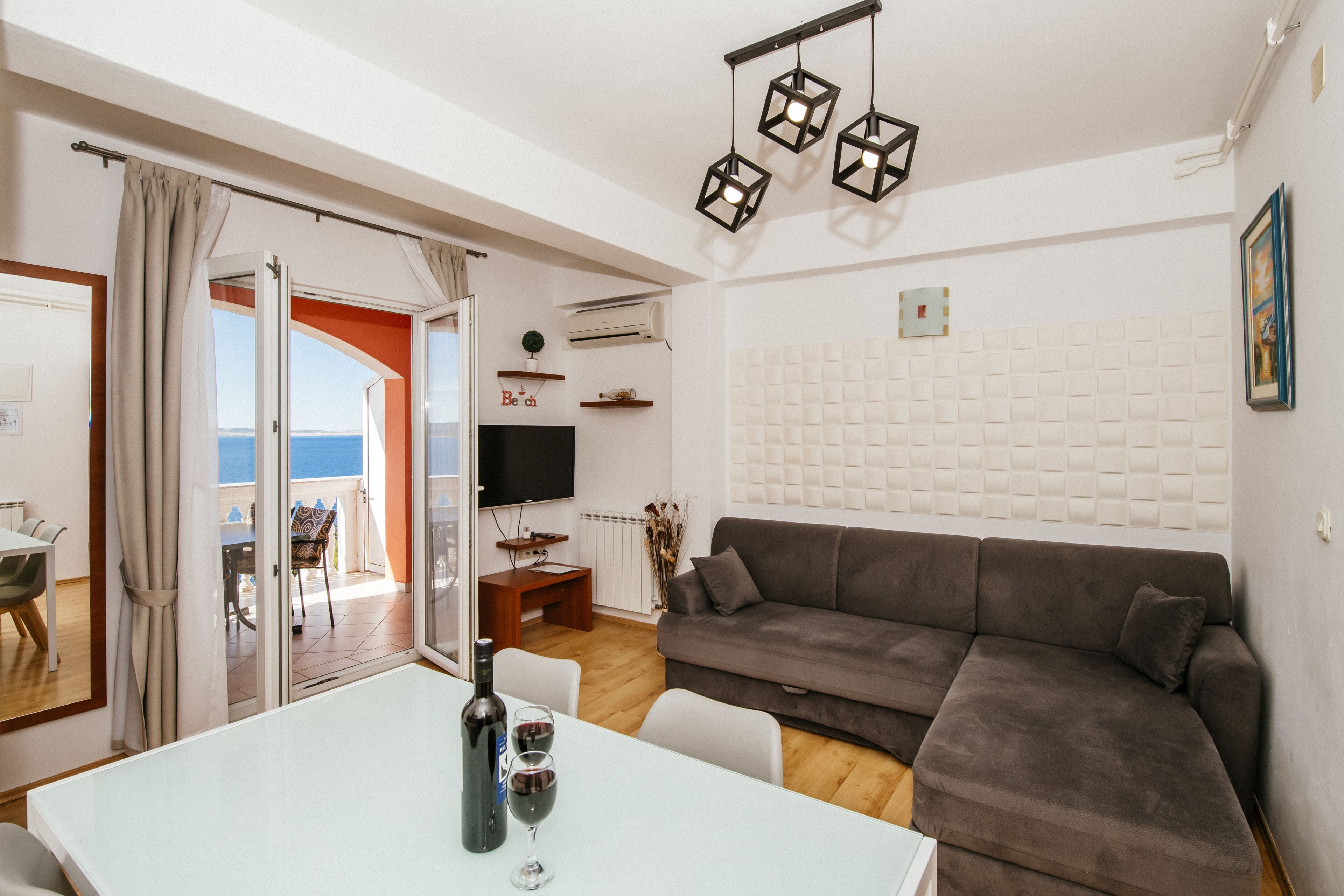 Un salon moderne avec un canapé gris, une table à manger avec des verres à vin et un téléviseur.