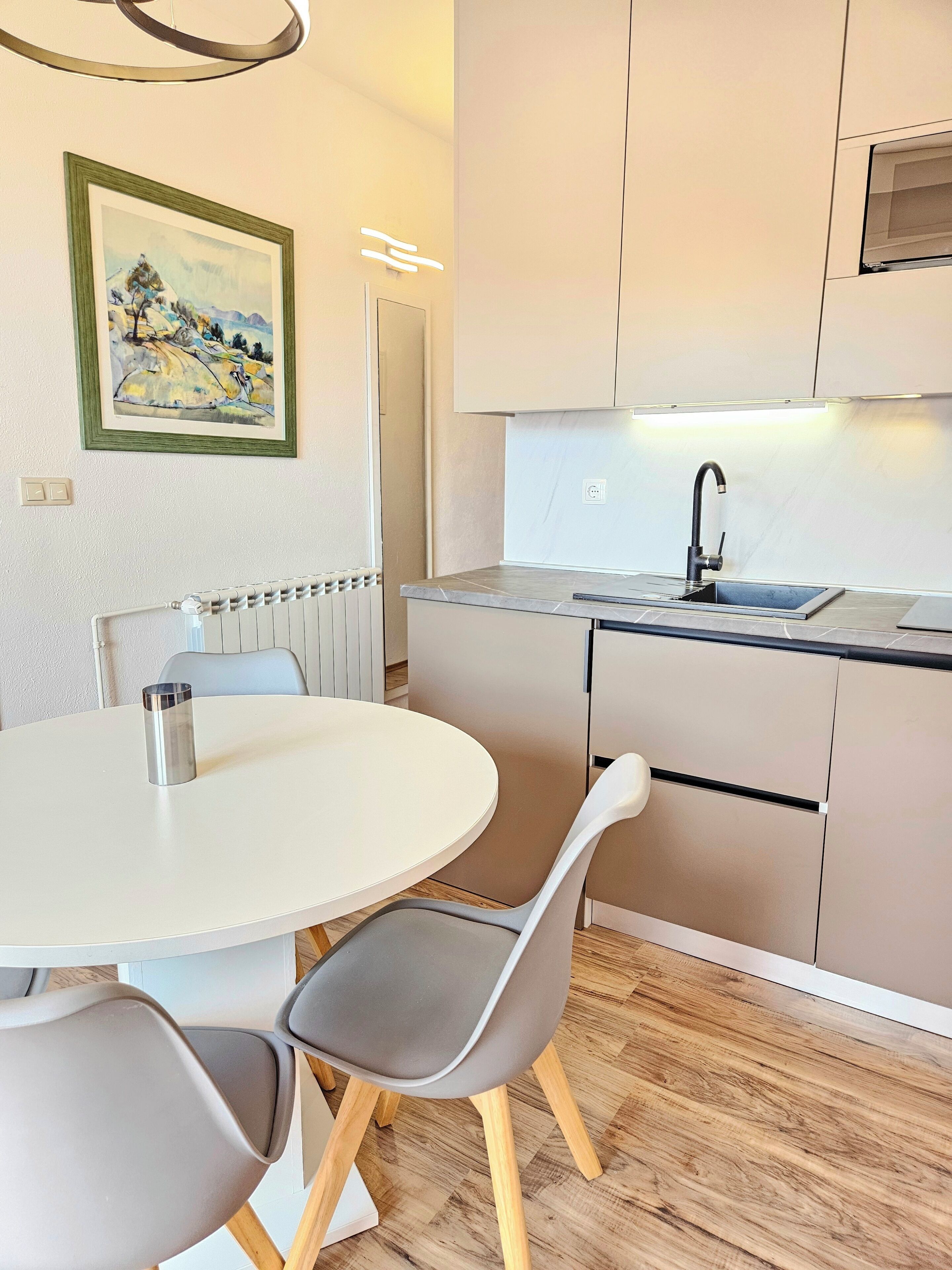 A modern kitchen with a round dining table, grey chairs, and a built-in sink.