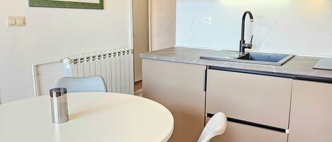 A modern kitchen with a round dining table, grey chairs, and a built-in sink.