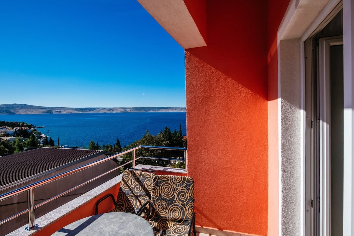 A balcony with a view of the sea, a patterned chair, and a metal railing.