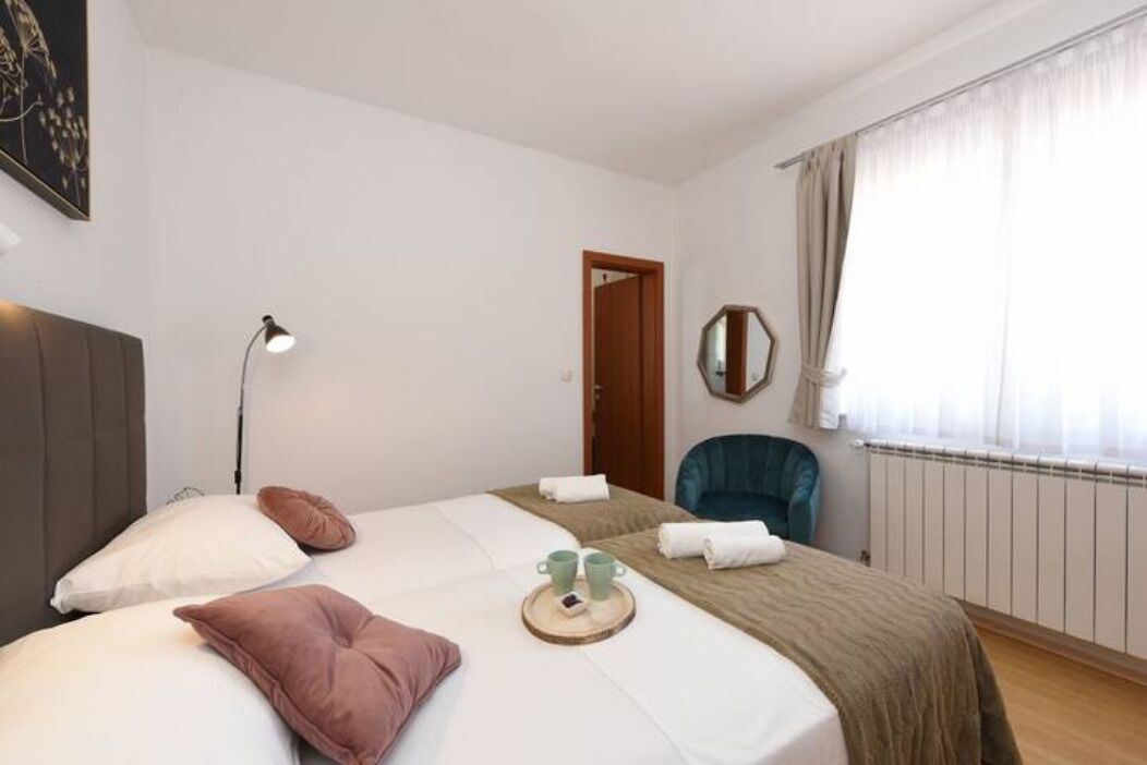 Et hotelværelse med seng, sengebordlampe, stol, vindue med gardiner og dør.