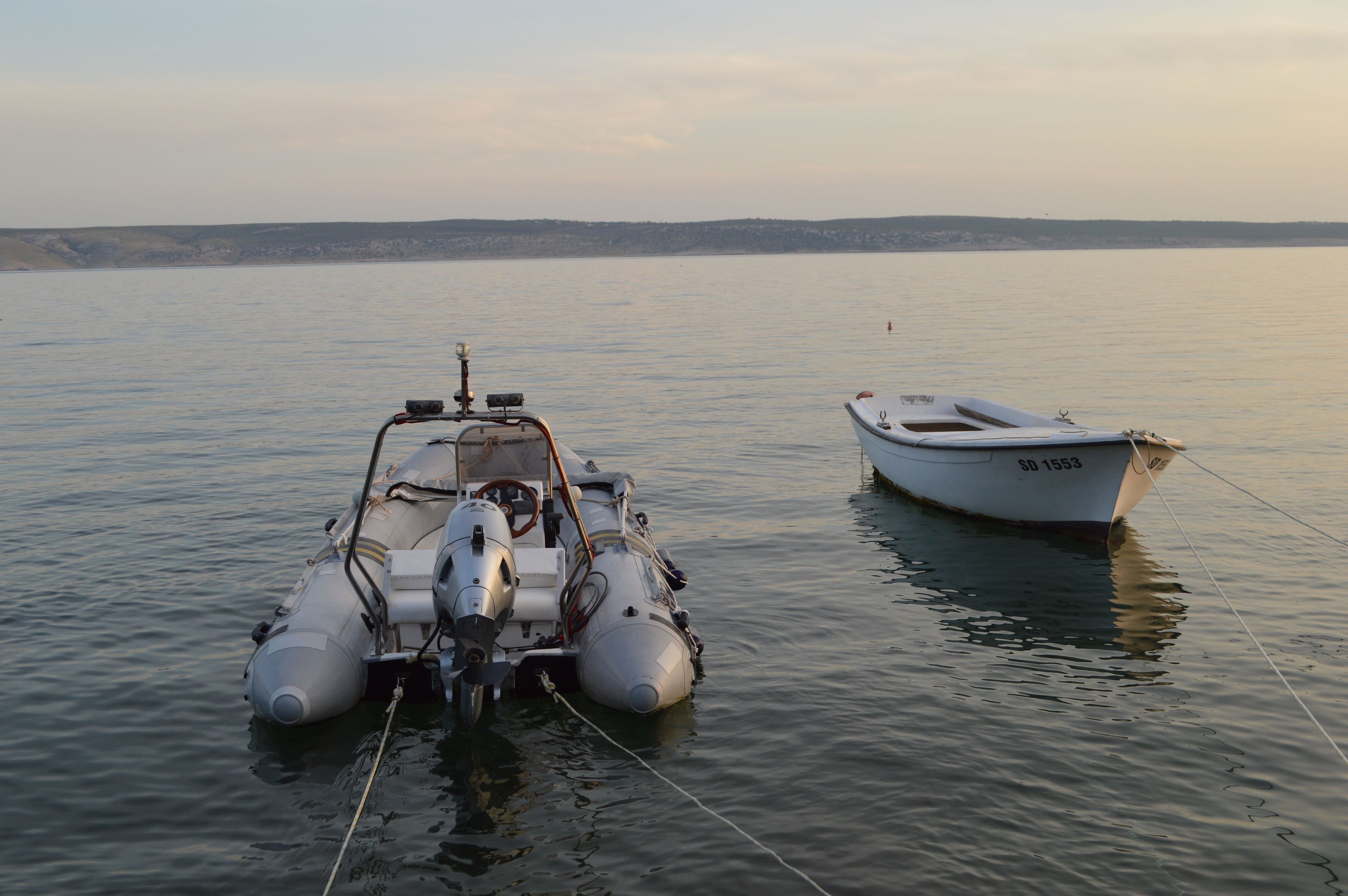A small motorboat tied to a larger vessel in calm waters.