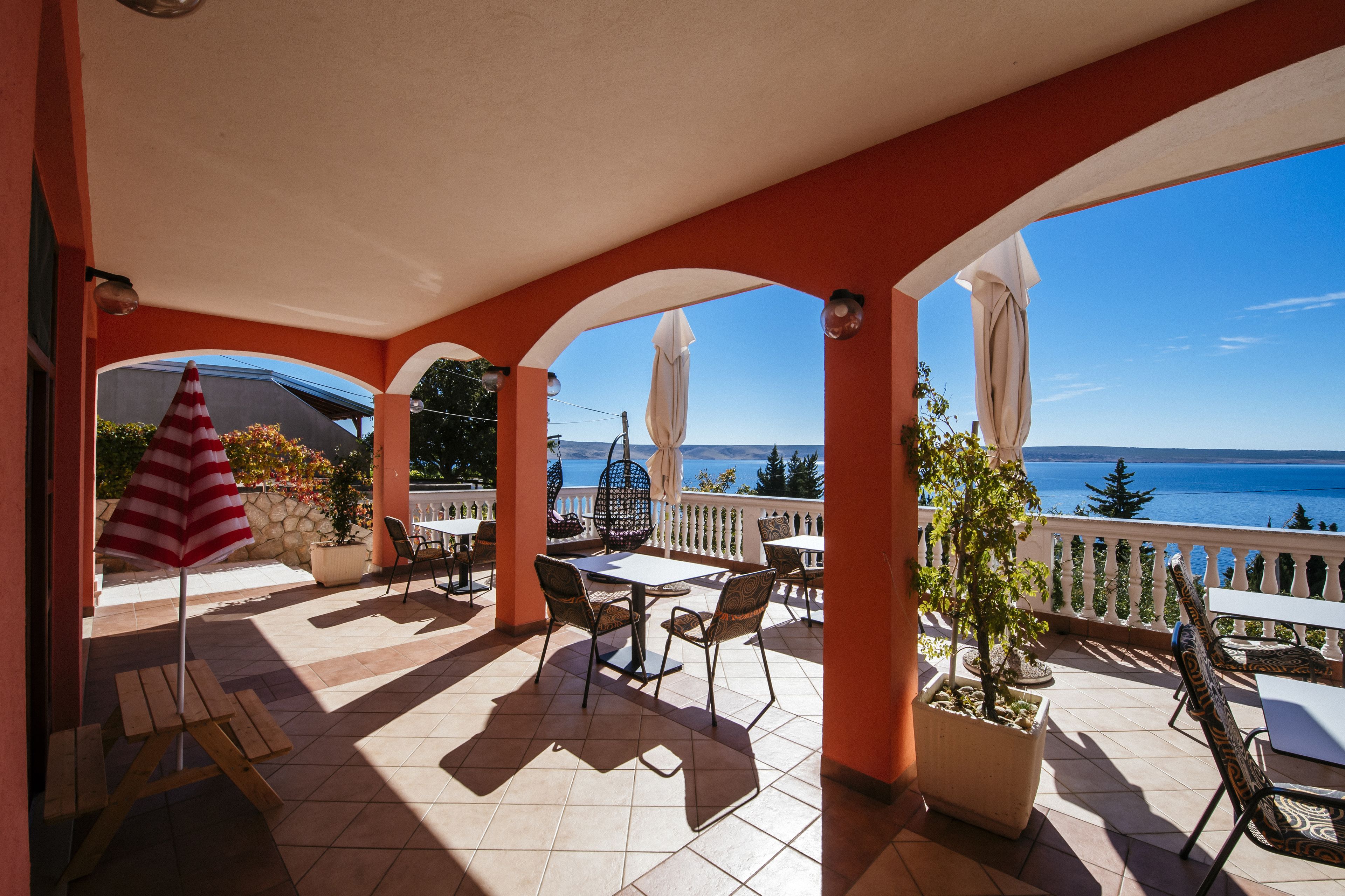 A covered patio with outdoor seating, a view of the sea, and a potted plant.