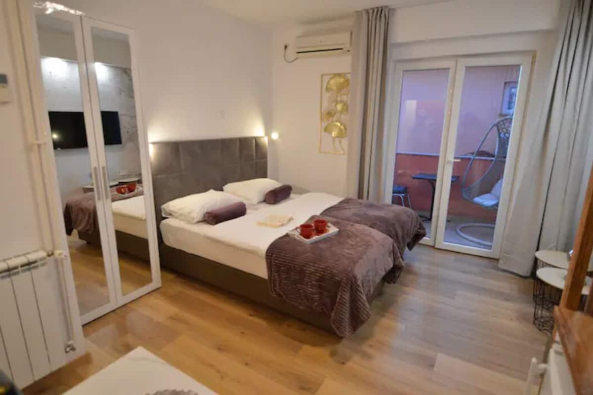A bedroom with a bed, a sliding glass door to a balcony, and a small table with a chair.
