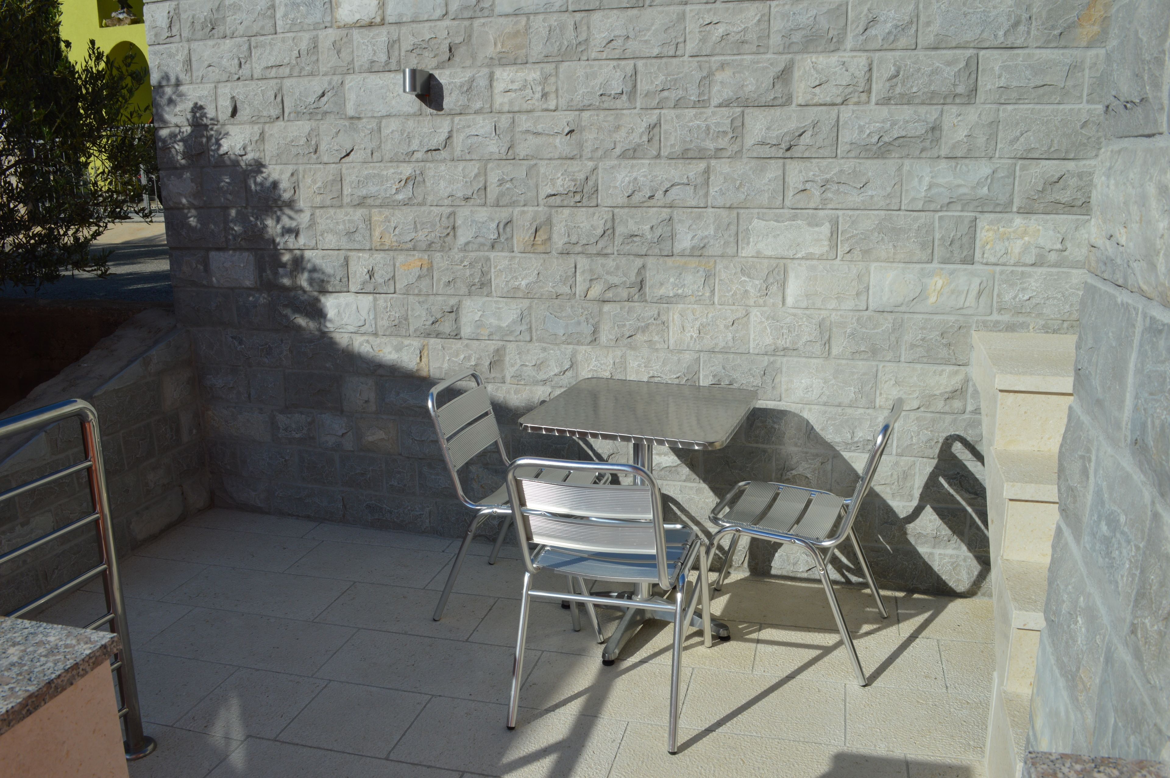 Une terrasse extérieure avec une table et des chaises, des murs en pierre et une rambarde en métal.