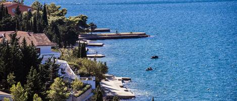 A coastal area with a pier extending into the sea, surrounded by residential buildings and dense greenery.