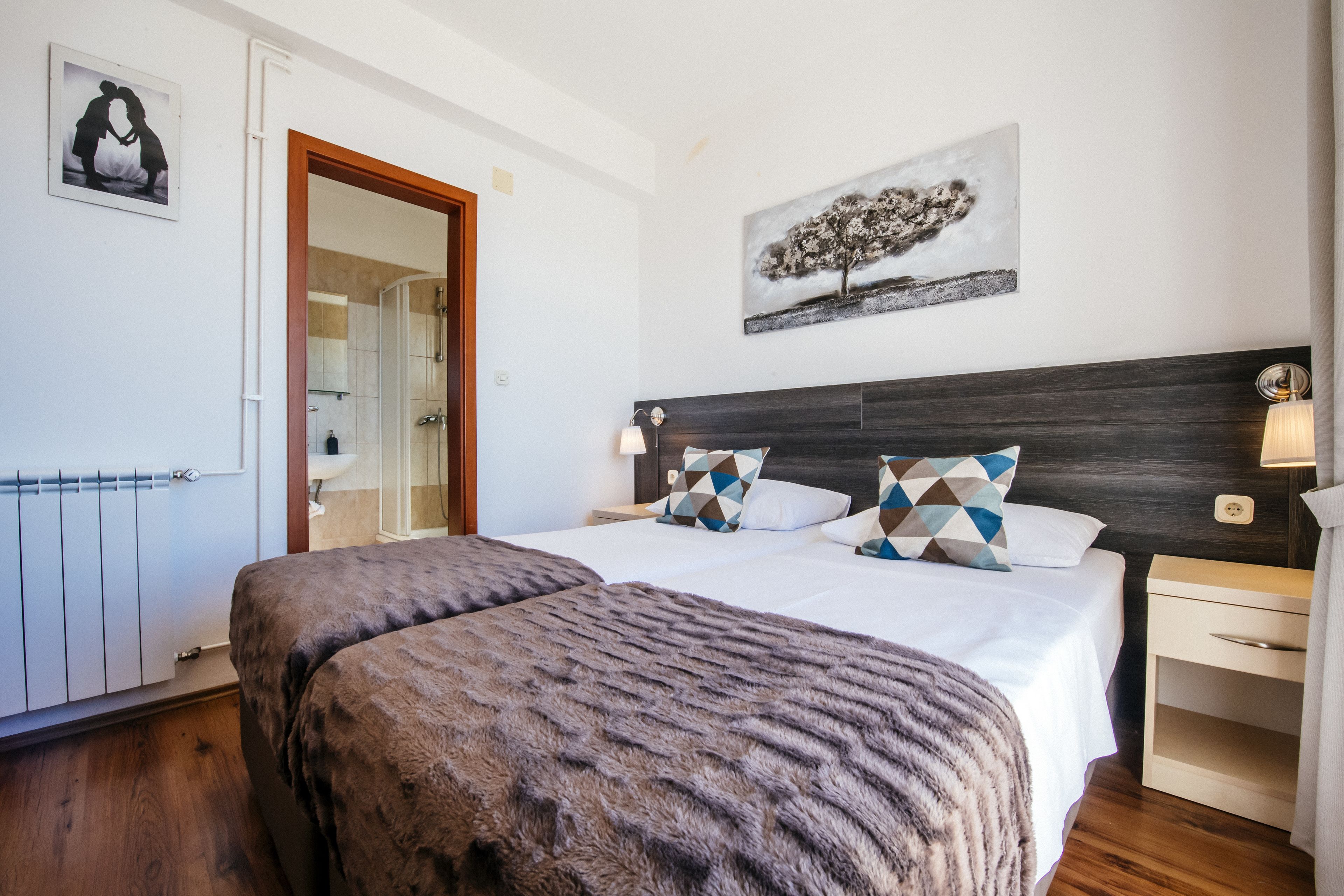 A bedroom with a large bed, a wooden headboard, a nightstand, a mirror, and a painting on the wall.