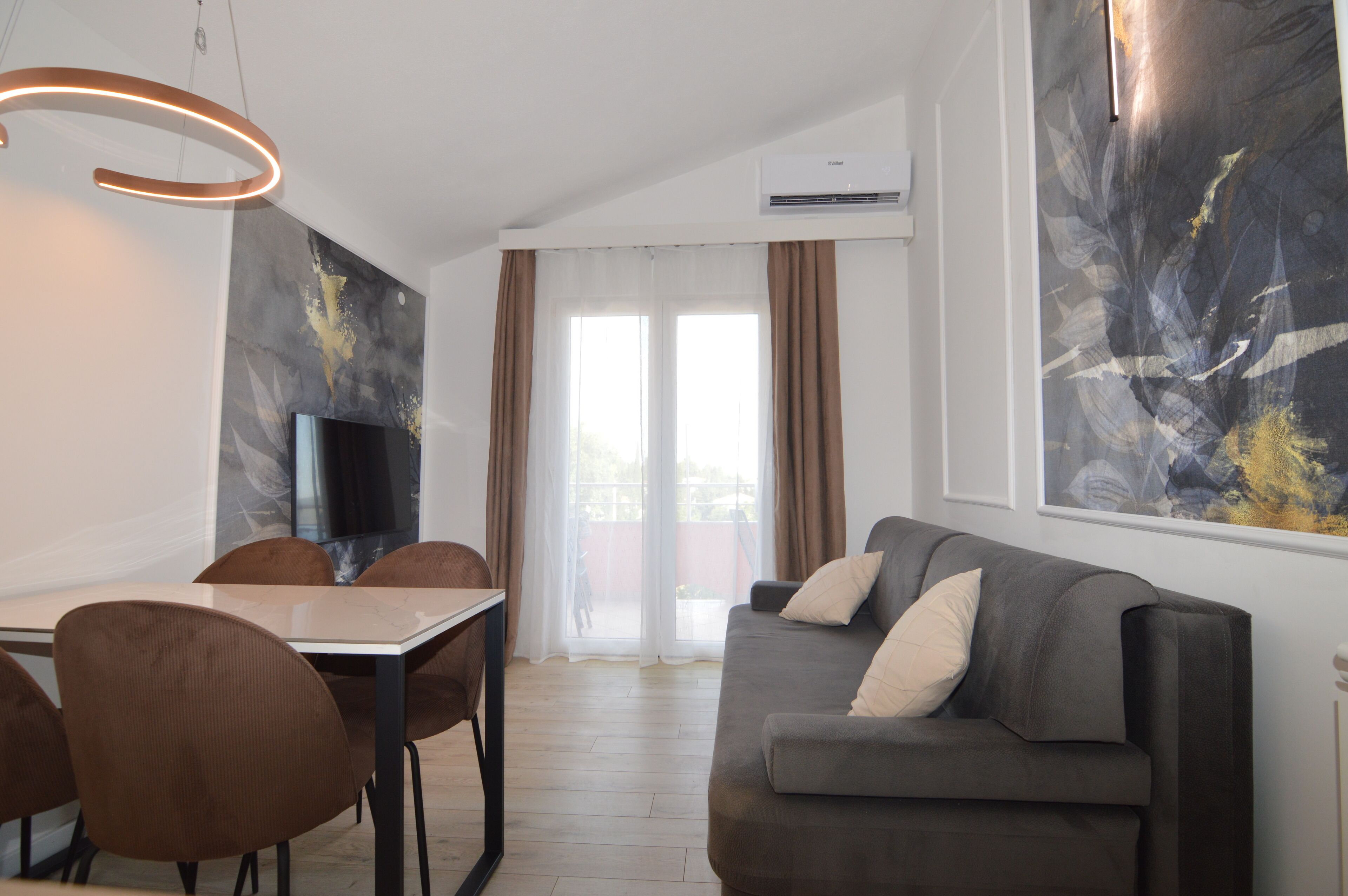 A modern living room with a grey sofa, brown chairs, a dining table, and a TV.