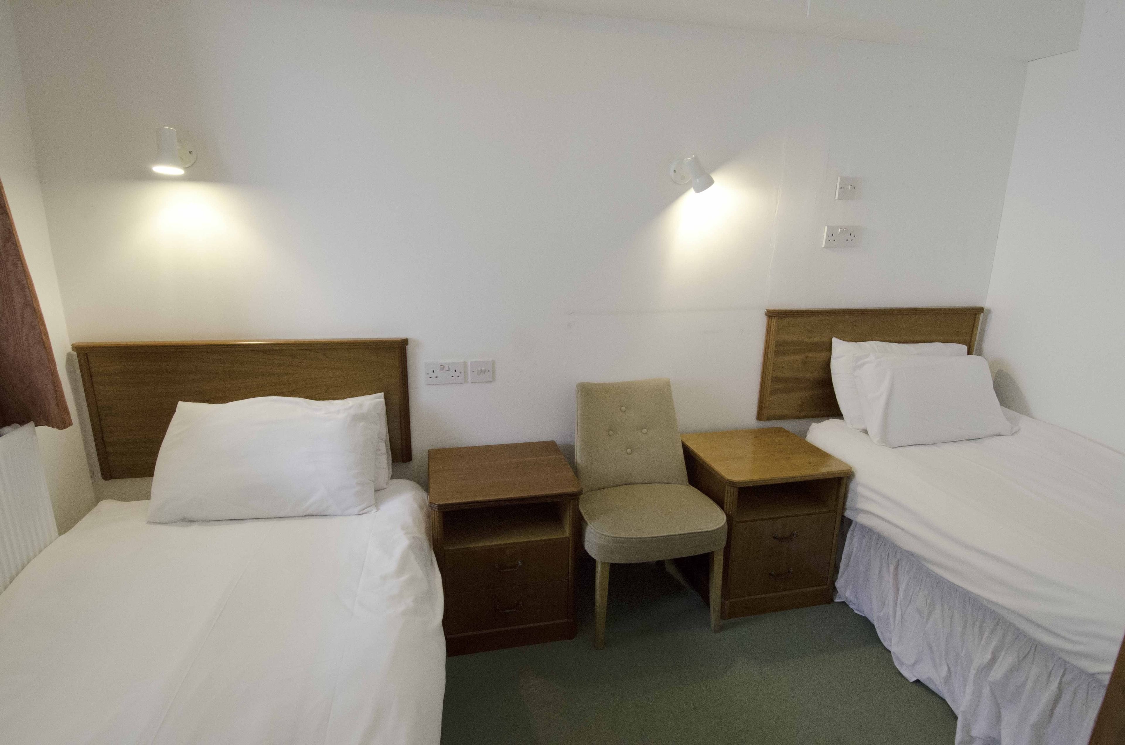 A hotel room with two beds, a chair, and two nightstands.