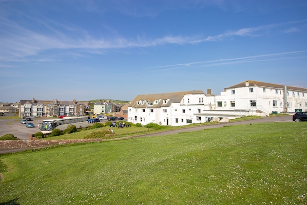 A residential area with white buildings, a grassy field, and parked cars. - Seacote Hotel (St Bees)