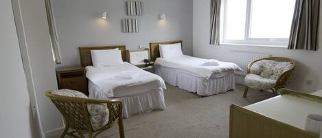 Een hotelkamer met twee enkele bedden, een houten stoel, een bureau en een raam met gordijnen.