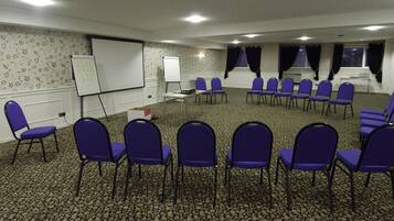 A conference room with a carpeted floor, whiteboard, projector, and rows of purple chairs.
