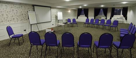 A conference room with a carpeted floor, whiteboard, projector, and rows of purple chairs.