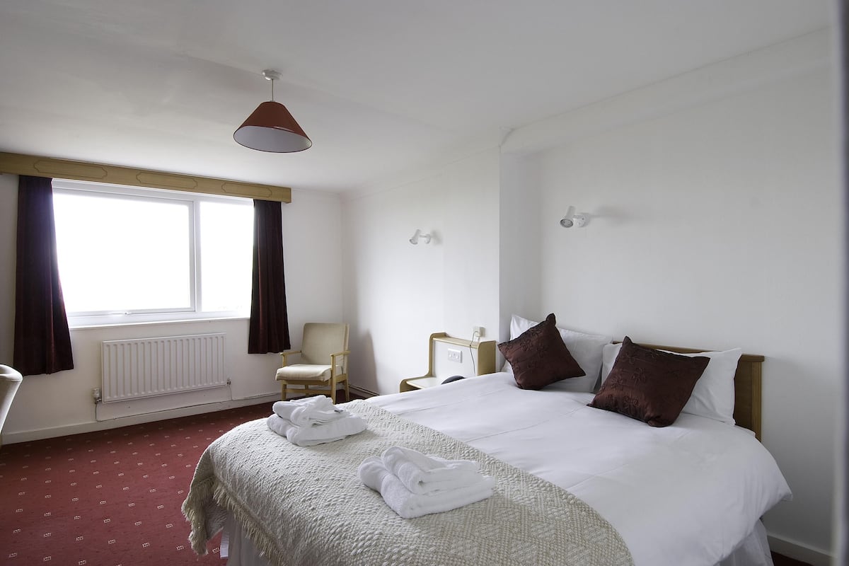 A hotel room with a large bed, a chair, a desk, and a window with curtains.