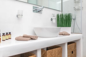 Un baño con un lavabo blanco, un espejo, un perchero para toallas y una zona de ducha.