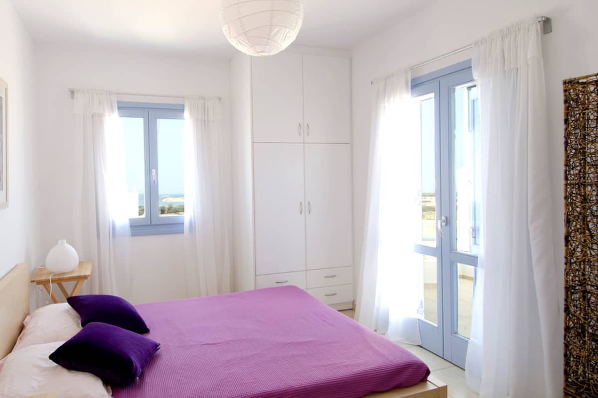 A bedroom with a bed, a nightstand, a wardrobe, and a window with curtains.