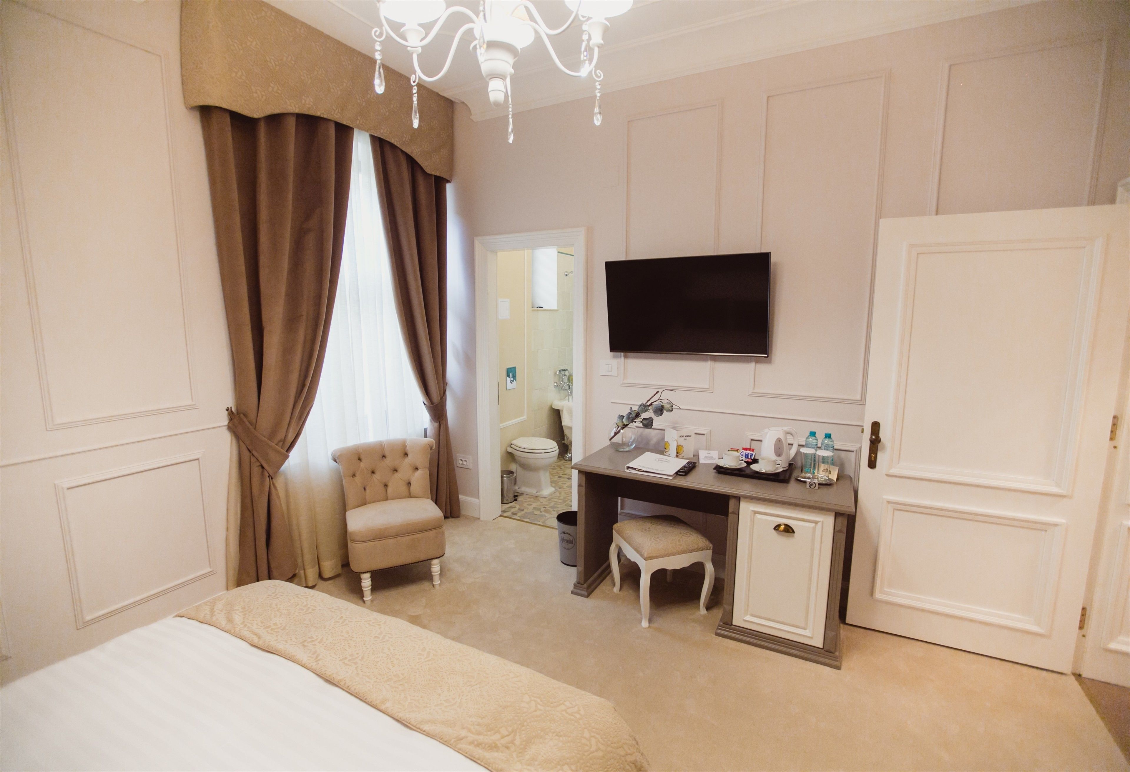 A hotel room with a bed, a desk with a chair, a television, and a door.