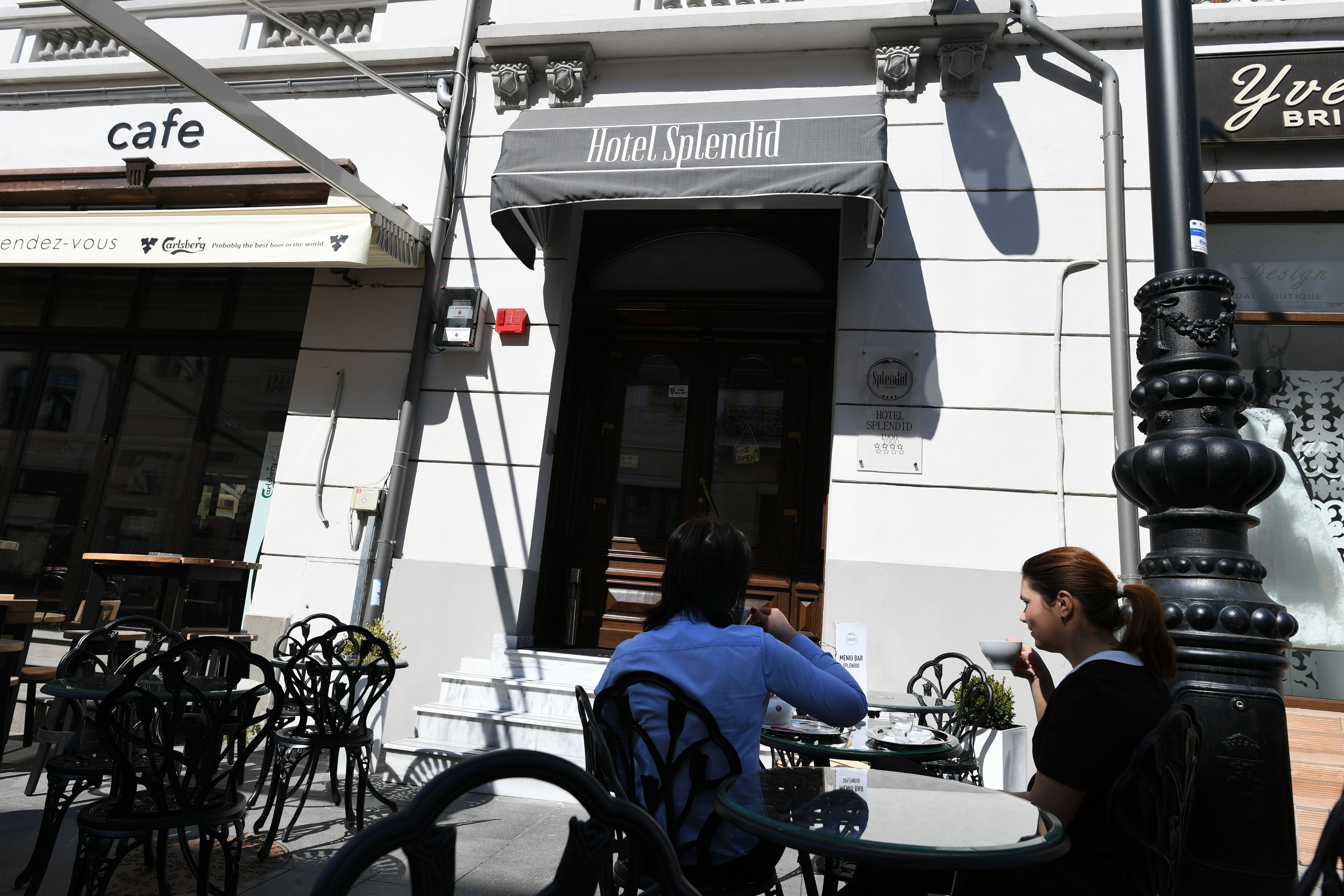 Un área de café al aire libre con mesas y sillas, un edificio con un letrero que dice 'Hotel Splendid' y un letrero de 'café' al fondo.