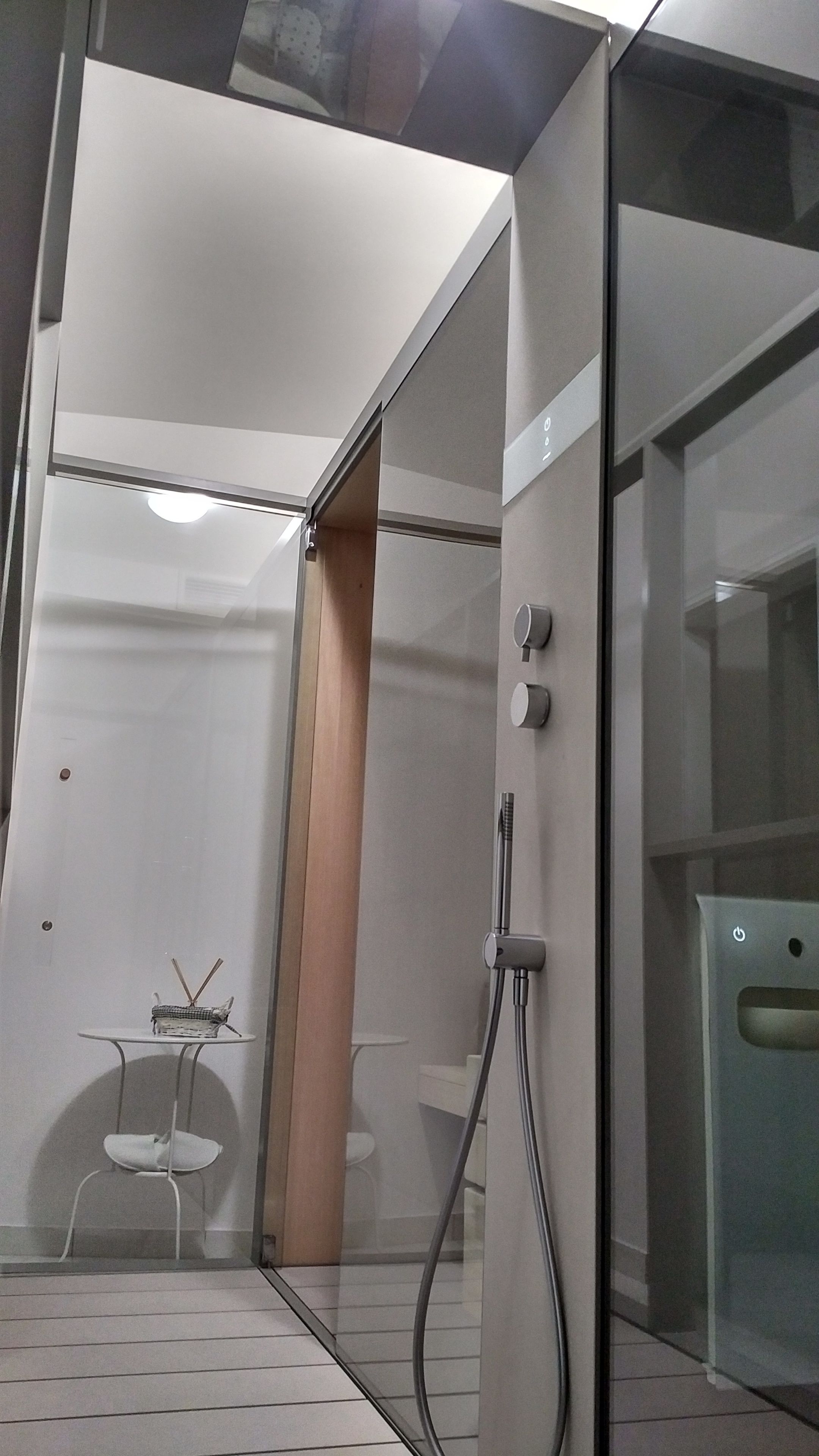 A modern bathroom with a glass shower enclosure, a small table with a chair, and a towel rack.