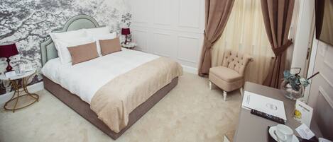 A hotel bedroom with a large bed, a chandelier, a sitting area with a chair, and a desk with a vase of flowers.