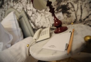 Una mesita de noche de mármol con un teléfono blanco, una lámpara roja, un bloc de notas y un lápiz.