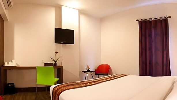 Une chambre d’hôtel avec un lit, un bureau, une chaise, une télévision et une fenêtre avec des rideaux.