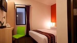Une chambre d’hôtel avec un lit, un bureau et une chaise, une fenêtre avec des rideaux et une lampe.