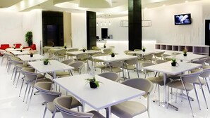 Une salle de conférence moderne, dotée de tables et de chaises blanches, d’un grand écran et d’un espace d’accueil.