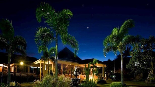Uma casa moderna com entrada bem iluminada, cercada por vegetação exuberante e palmeiras.