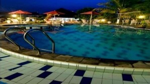 Piscina com deck ladrilhado, rodeada por palmeiras e guarda-sóis vermelhos.